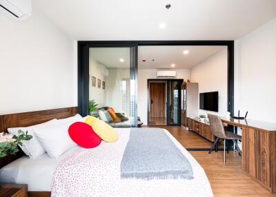 Modern bedroom with cozy bed, work desk, and sliding glass doors leading to a well-lit interior space