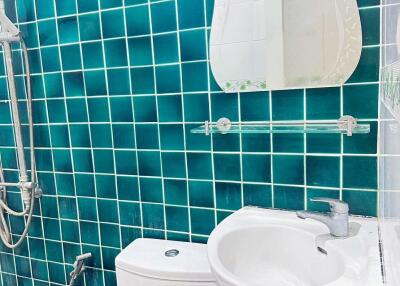 Bathroom with teal tiled walls, white fixtures, and glass mirror