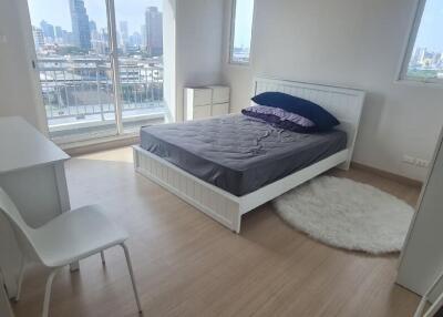 Bedroom with bed, desk, chair, and large windows with city view