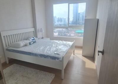 Bright bedroom with a large window, a bed with white frame, bedside tables, and a city view