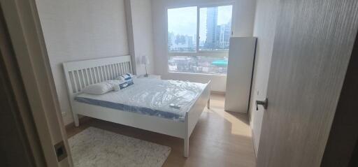 Bright bedroom with a large window, a bed with white frame, bedside tables, and a city view