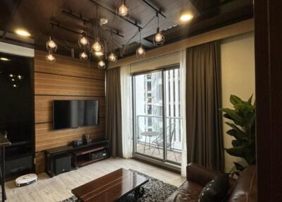 Modern living room with brown leather couch, TV on wooden accent wall, coffee table, and large window with curtains