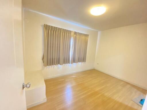 Spacious empty bedroom with hardwood floor and window with curtains