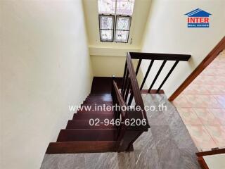 Indoor staircase with wooden steps and railing, window, and tiled flooring at the bottom.