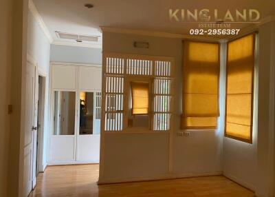 Living room with wooden floors, large windows with yellow shades, and an area with white louvers separating spaces