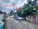 Street view with cars parked, trees, and a sign with contact information