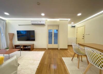 Modern living room with wooden flooring, television, dining table, and air conditioning.