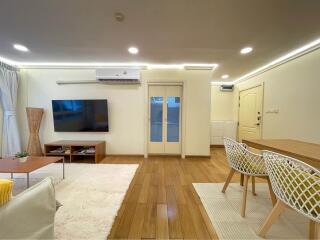 Modern living room with wooden flooring, television, dining table, and air conditioning.