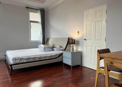 Spacious bedroom with wooden flooring, bed, and a small table with a chair.