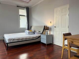 Spacious bedroom with wooden flooring, bed, and a small table with a chair.