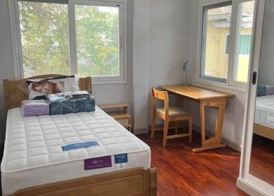 A cozy bedroom with a single bed, desk, and large windows