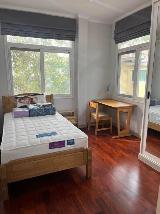 A cozy bedroom with a single bed, desk, and large windows