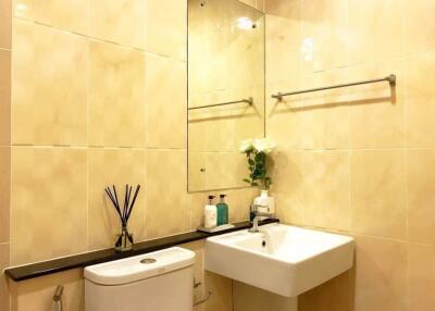 Modern beige-tiled bathroom with sink, toilet, and vanity mirror