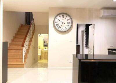 Main living area with wall clock, stairs to the second floor, and a view of a hallway leading to a bathroom