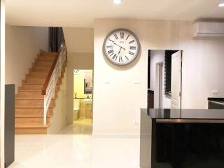 Main living area with wall clock, stairs to the second floor, and a view of a hallway leading to a bathroom