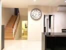 Main living area with wall clock, stairs to the second floor, and a view of a hallway leading to a bathroom