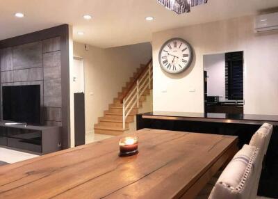 Modern living room with wooden dining table, wall clock, staircase, and wall-mounted TV