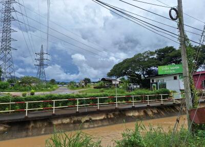 View of an outdoor area featuring a water canal, electrical towers, and vegetation along with some small structures.