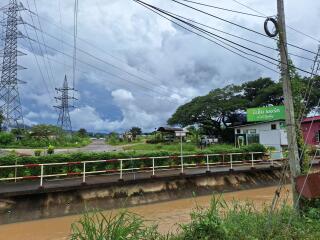 View of an outdoor area featuring a water canal, electrical towers, and vegetation along with some small structures.