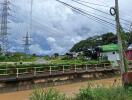 View of an outdoor area featuring a water canal, electrical towers, and vegetation along with some small structures.