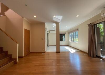 Spacious living area with wooden flooring, staircase, and large windows