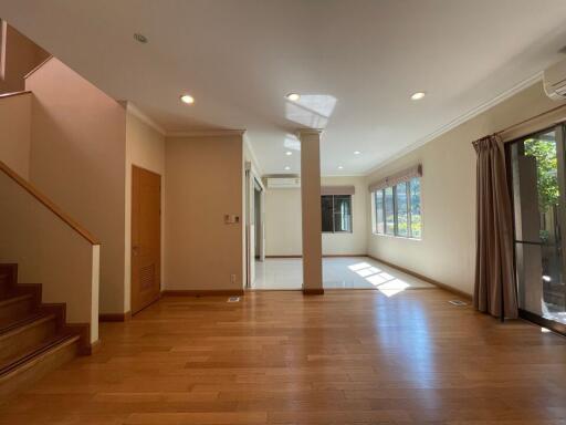 Spacious living area with wooden flooring, staircase, and large windows