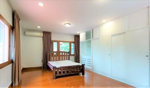 Spacious bedroom with wooden flooring, a large bed, built-in wardrobe, and windows with curtains