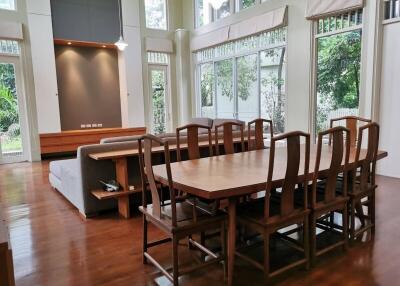 Spacious living room with wooden dining table, ample seating, large windows, and wooden flooring