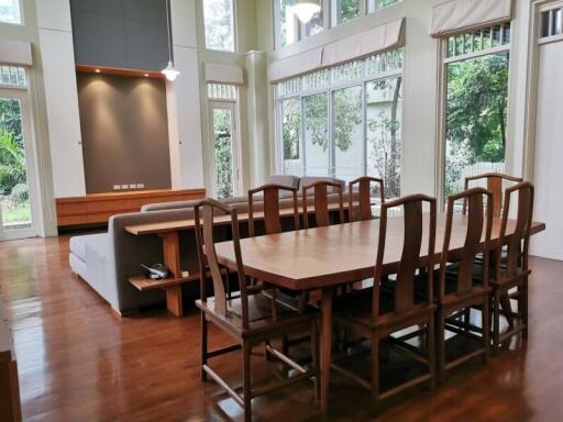 Spacious living room with wooden dining table, ample seating, large windows, and wooden flooring