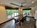 Spacious dining room with large table and chairs, featuring a ceiling fan and large windows offering plenty of natural light