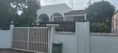 Front view of a house with surrounding greenery and a white gate