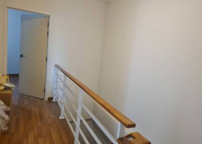 A bright hallway with wooden flooring and a white railing