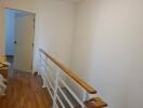 A bright hallway with wooden flooring and a white railing