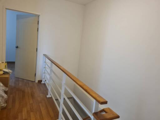 A bright hallway with wooden flooring and a white railing