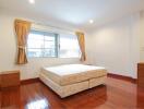 Bright bedroom with a large window, bed, nightstands, and wooden flooring