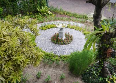 Beautiful outdoor garden with a central stone-paved circular area featuring a decorative birdbath surrounded by vibrant plants