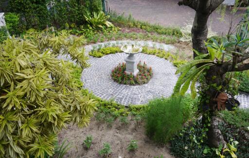 Beautiful outdoor garden with a central stone-paved circular area featuring a decorative birdbath surrounded by vibrant plants