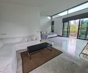 Modern living room with large windows, a white couch, a black coffee table, and visible sleeping area.