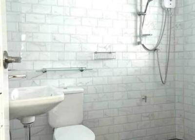 Clean white tiled bathroom with sink, toilet, and shower