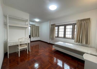 Spacious bedroom with wooden parquet flooring, single bed, desk, chair, and large windows with curtains.