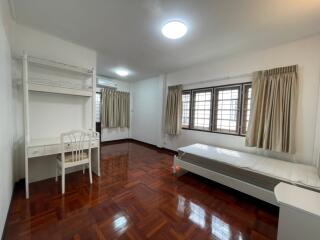 Spacious bedroom with wooden parquet flooring, single bed, desk, chair, and large windows with curtains.