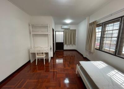 Spacious bedroom with wooden flooring, a bed, desk, and large windows