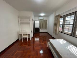 Spacious bedroom with wooden flooring, a bed, desk, and large windows