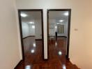 A view of a living space with two doorways leading to separate rooms, featuring wooden floors and white walls.