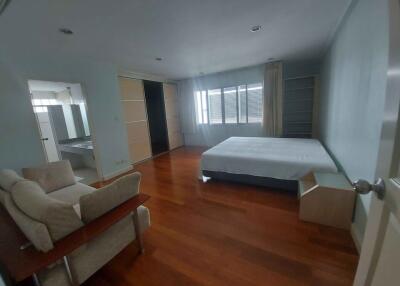 Spacious bedroom with wooden flooring, large windows, and comfortable sitting area