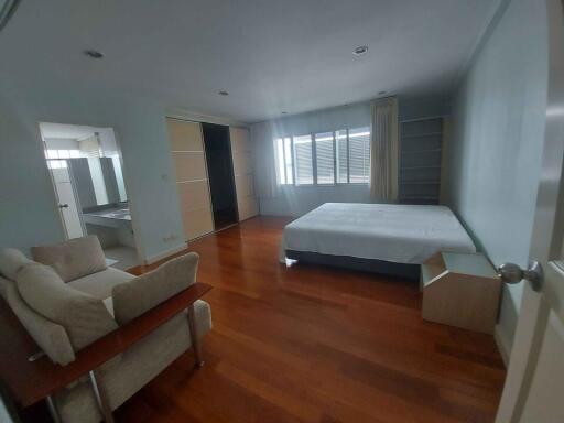 Spacious bedroom with wooden flooring, large windows, and comfortable sitting area