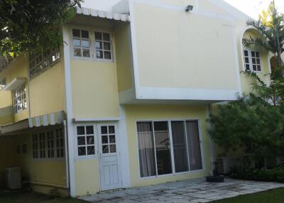 Exterior view of a two-story house with a yellow facade, white trim and windows, and surrounding greenery