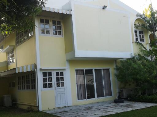 Exterior view of a two-story house with a yellow facade, white trim and windows, and surrounding greenery