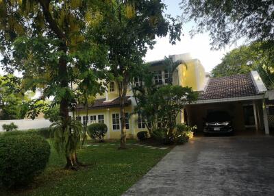 Front view of a two-story yellow house with a carport and garden