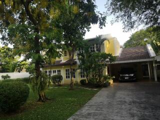 Front view of a two-story yellow house with a carport and garden